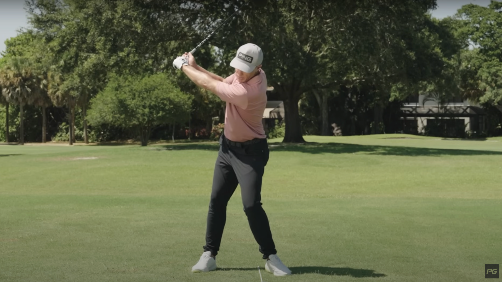 Photo of a man swinging a golf club mid-swing with an alignment stick on the ground.