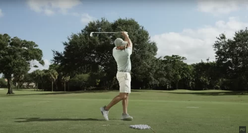 Performance Golf Coach Eric Cogorno on the golf course, mid swing with the golf club above his head and a pile of golf balls on the ground in front of him.