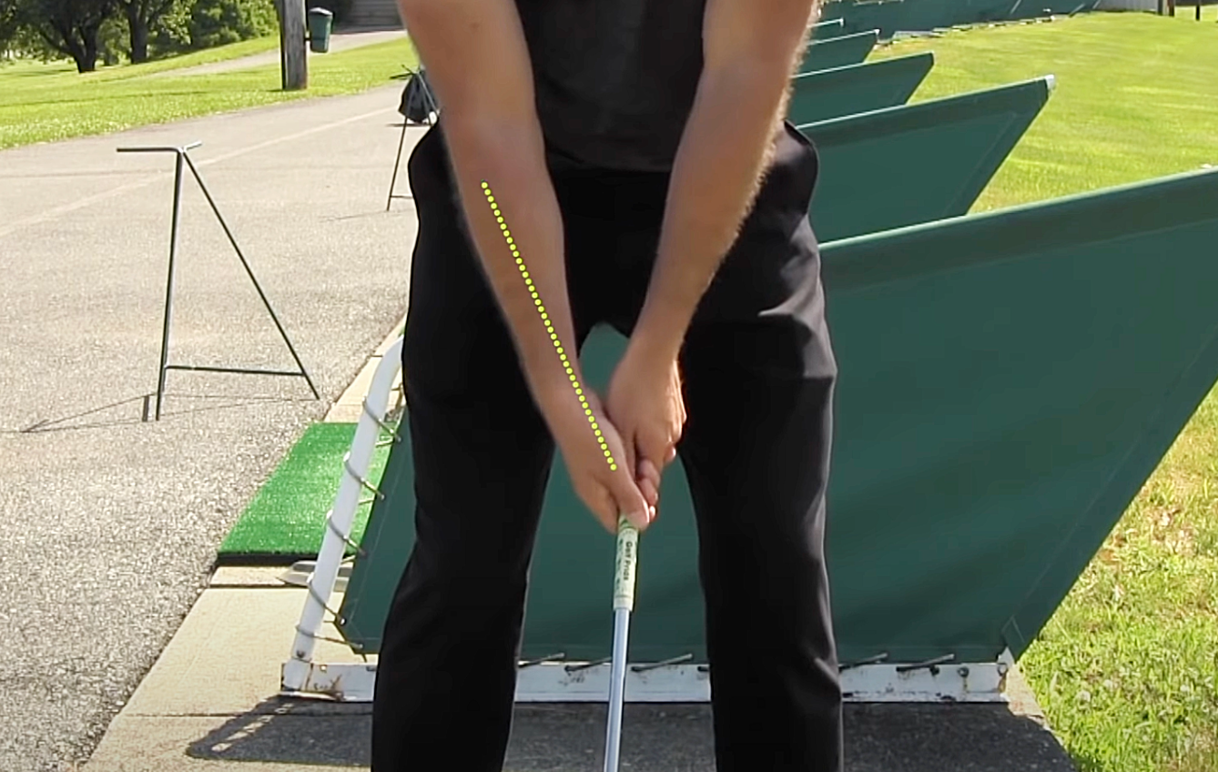 Shot from the elbows down of a golfer on the driving range, showcasing the grip of both hands on the golf club with a yellow dotted line showing the correct angle of the right forearm and hand.