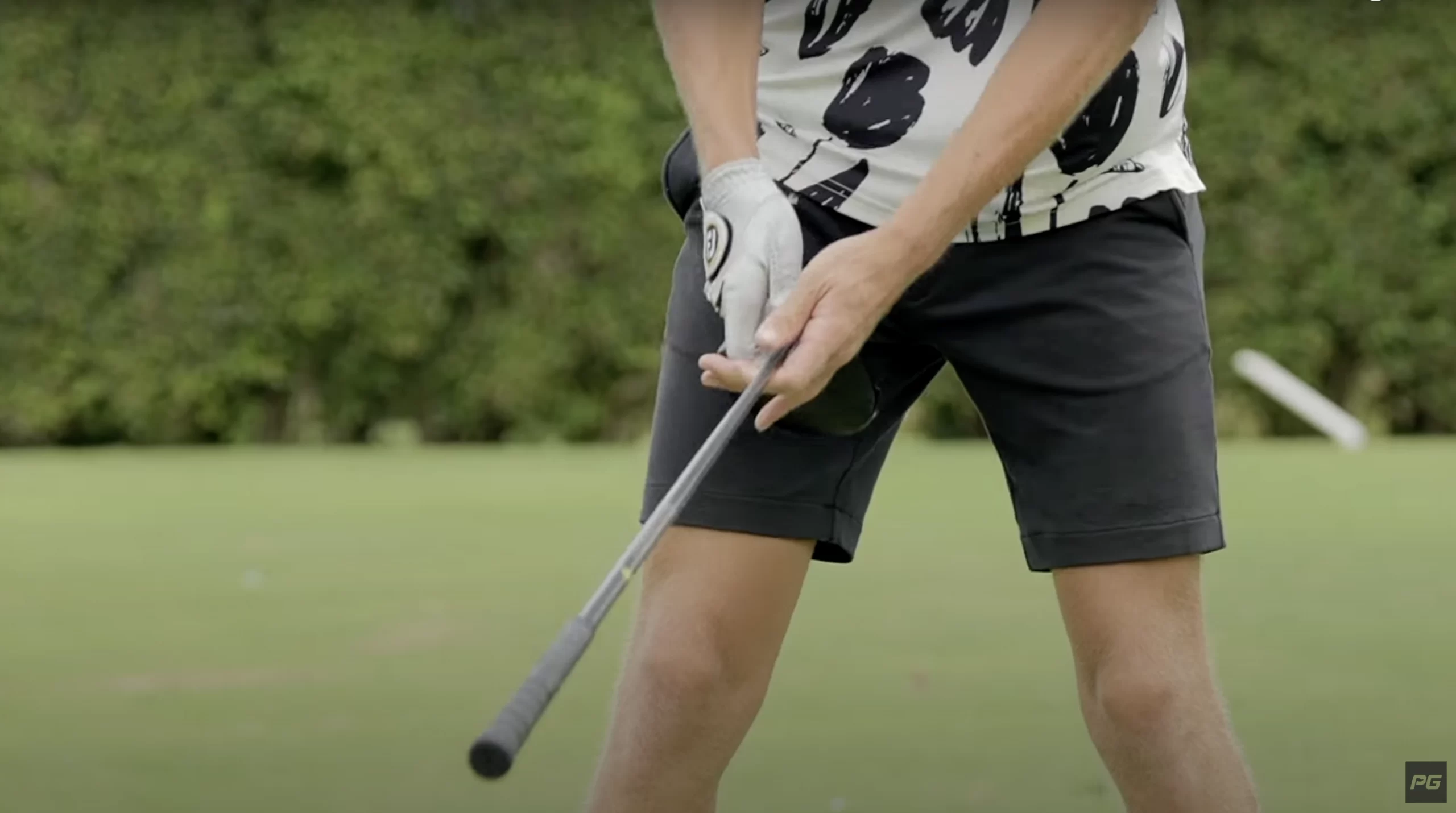 A golfer in the middle of a golf speed drill, holding the golf club backwards, with the club head in their hands and the grip at the end.