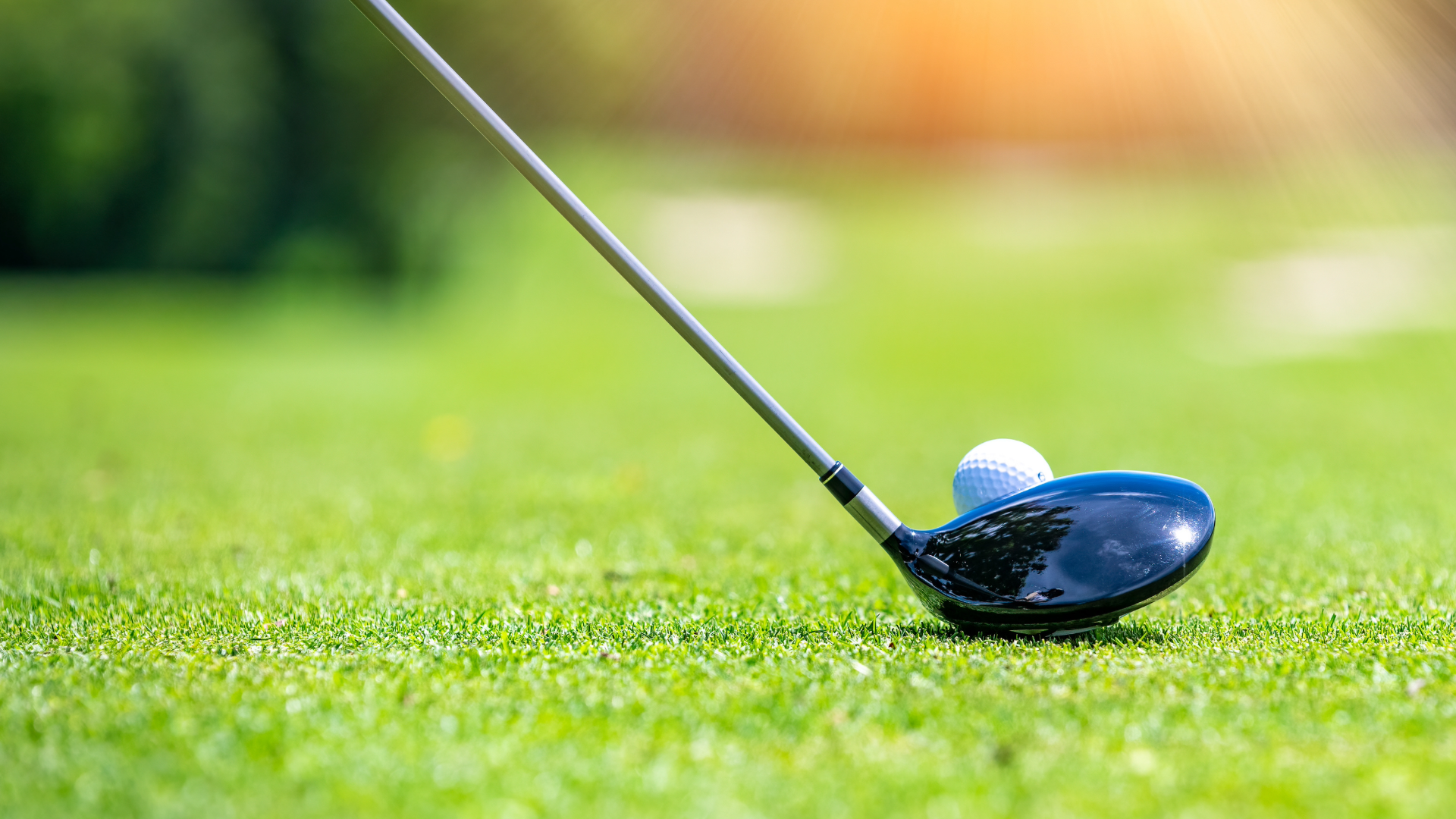 Close up of the grass and a golf ball on a tee with a golf driver.