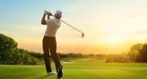 Golfer on the golf course at sunset swinging a golf driver.