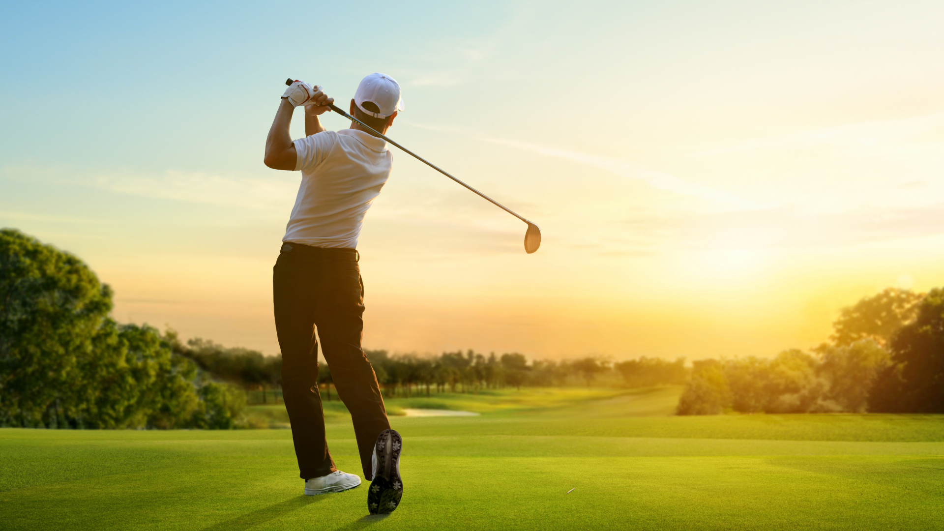 Golfer on the golf course at sunset swinging a golf driver.