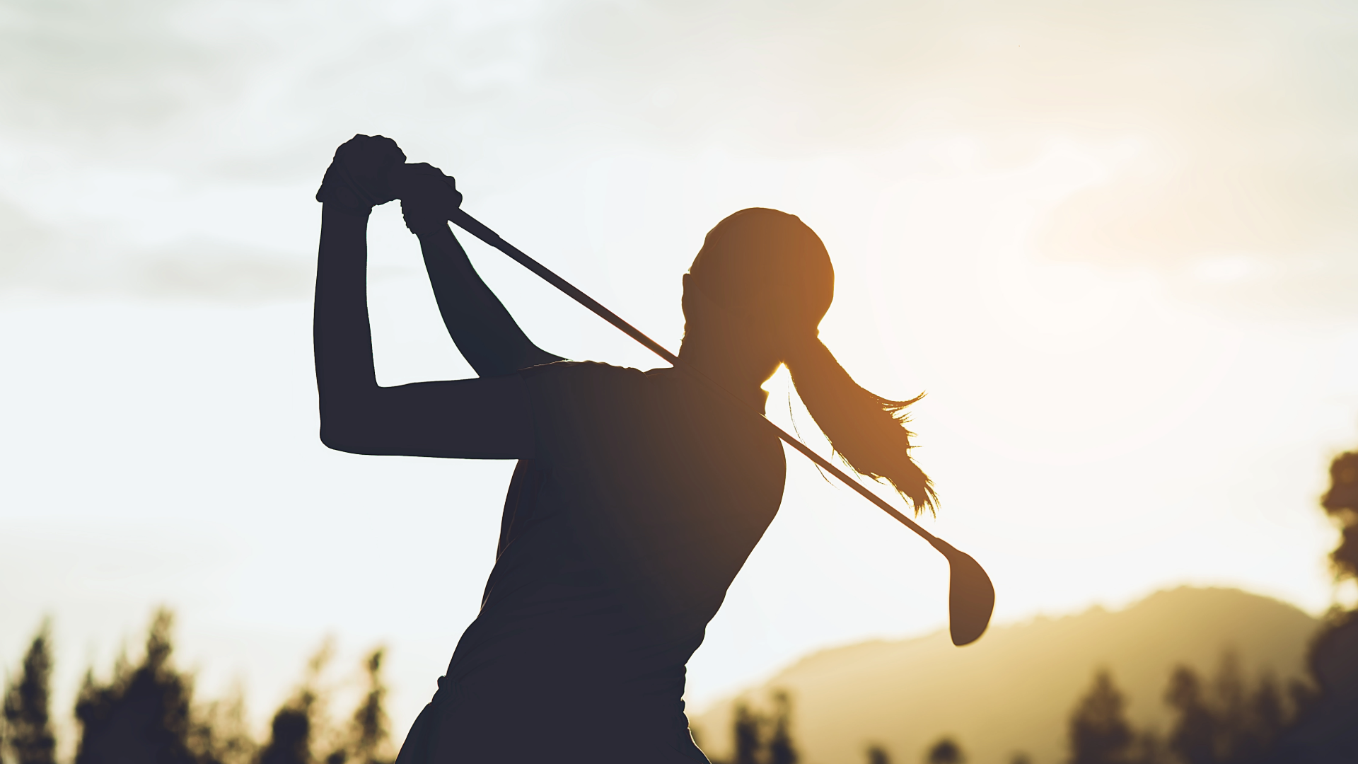 Silhouette of a woman on the golf course, mid golf swing.