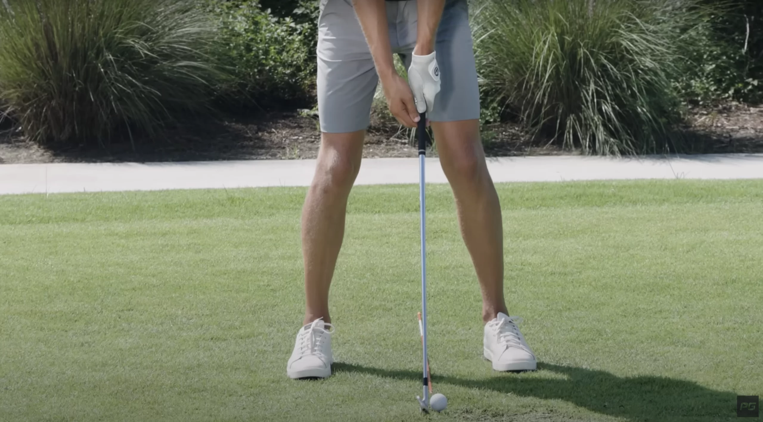 Golfer setting up their golf position with an iron and the golf ball slightly up in the stance.