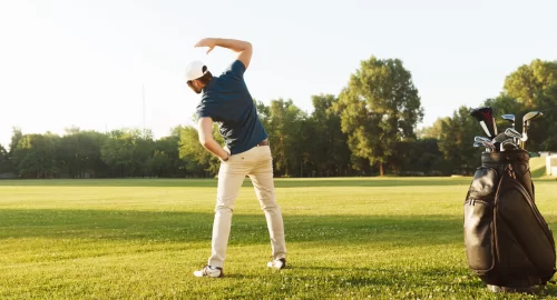 A man stretching on the golf course with his golf bag in the foreground.