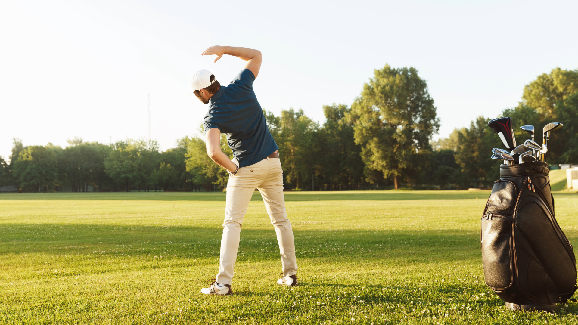 A man stretching on the golf course with his golf bag in the foreground.