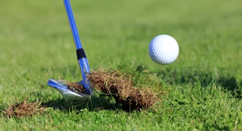 A wedge hitting a golf ball and turf mid swing.