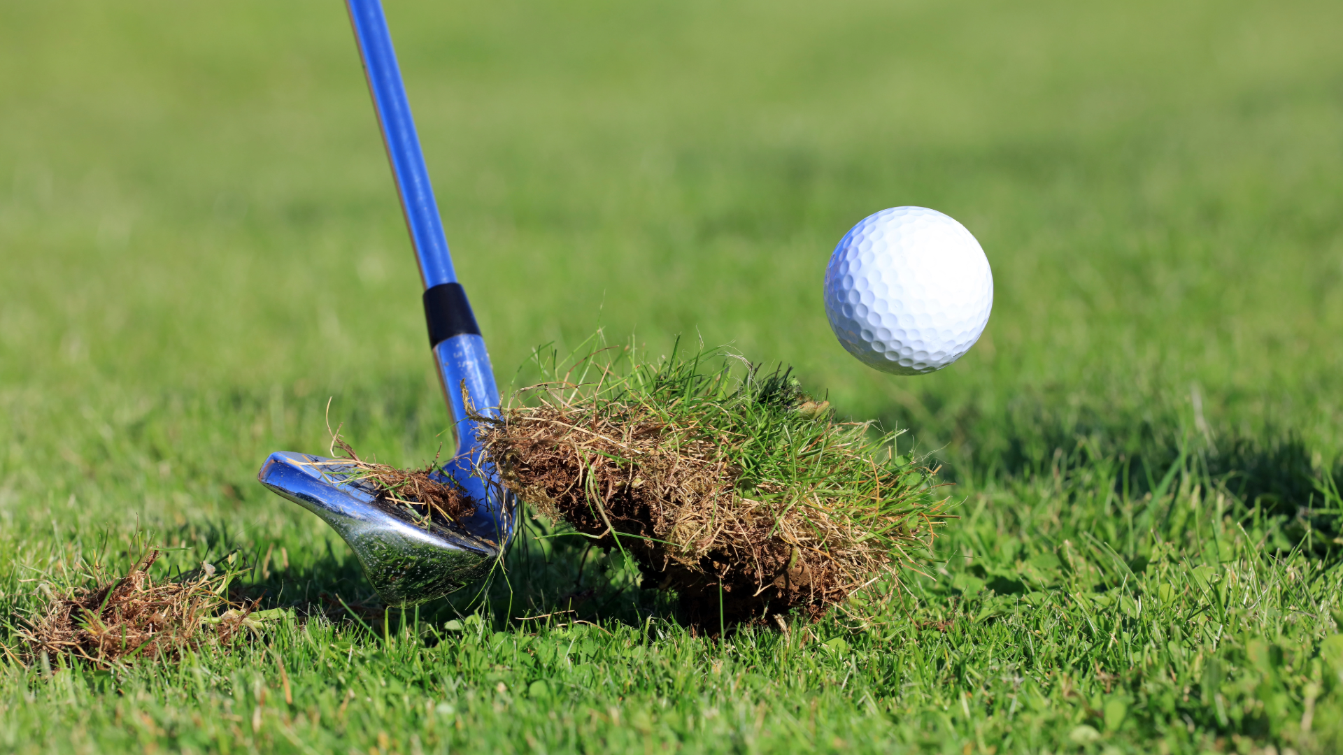 A wedge hitting a golf ball and turf mid swing.